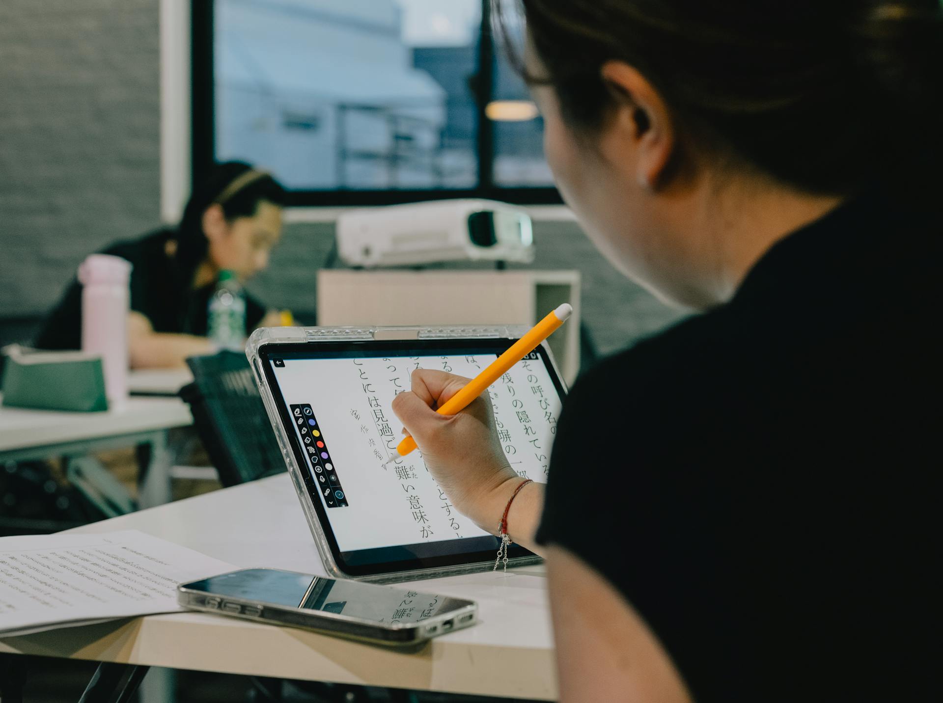 Student using a stylus on a tablet for notes in a bright classroom. Photo: Gu Ko / Pexels.