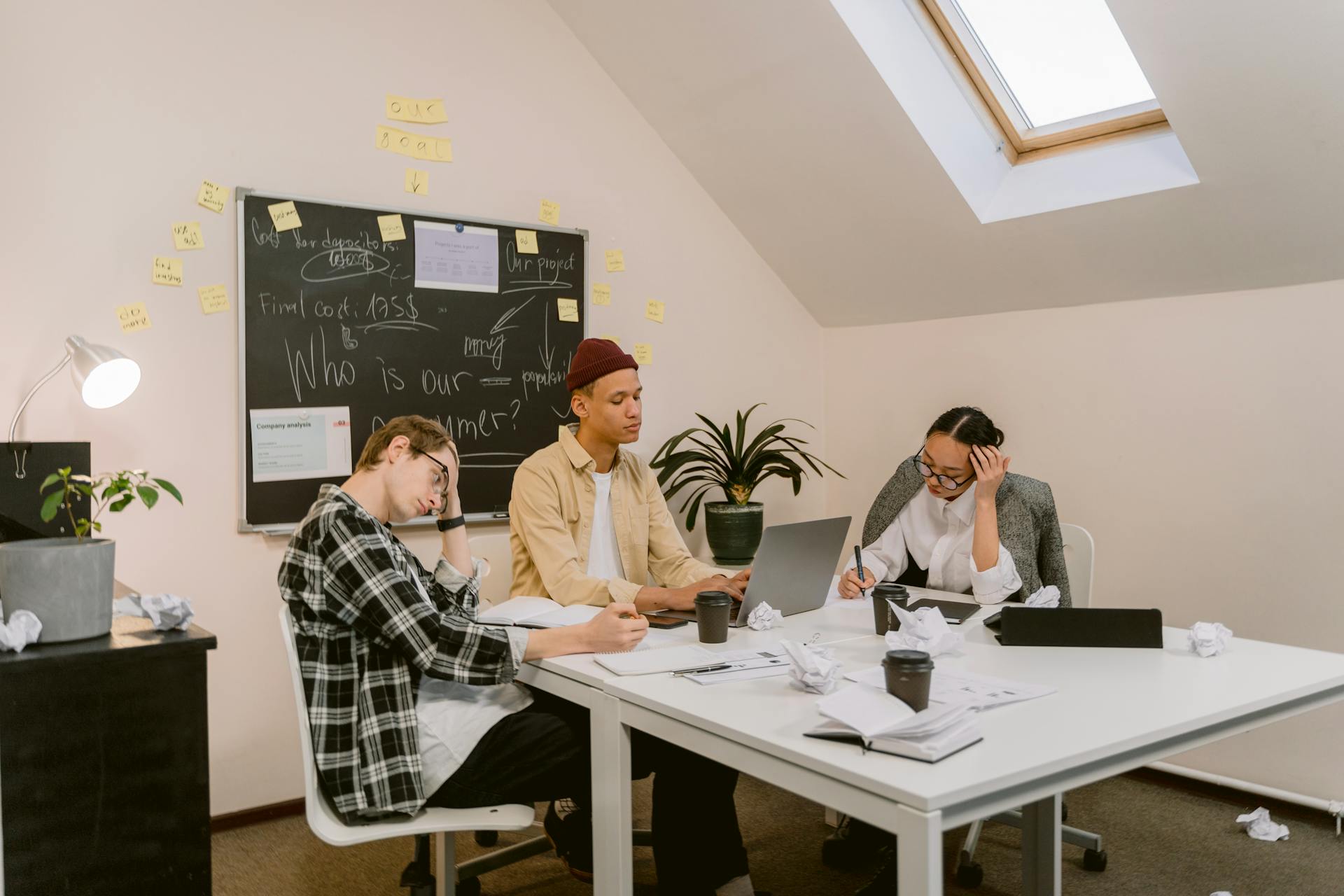 Postgraduate collaborators working with a laptop, notebooks, and chalkboard notes in a study space. Photo: Tima Miroshnichenko / Pexels.