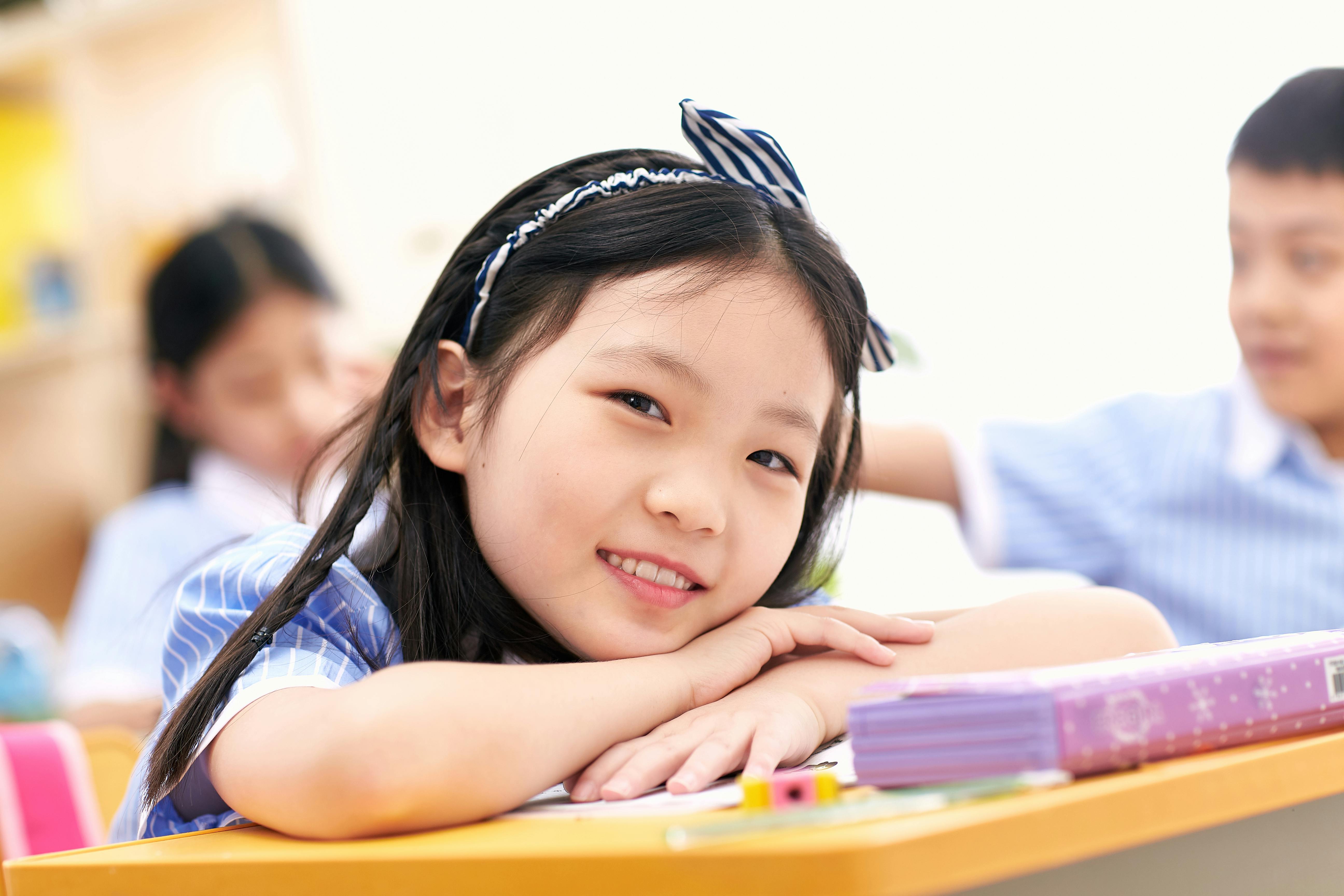 Primary school girl smiling at her desk in a bright classroom. Photo: Luyi / Pexels.