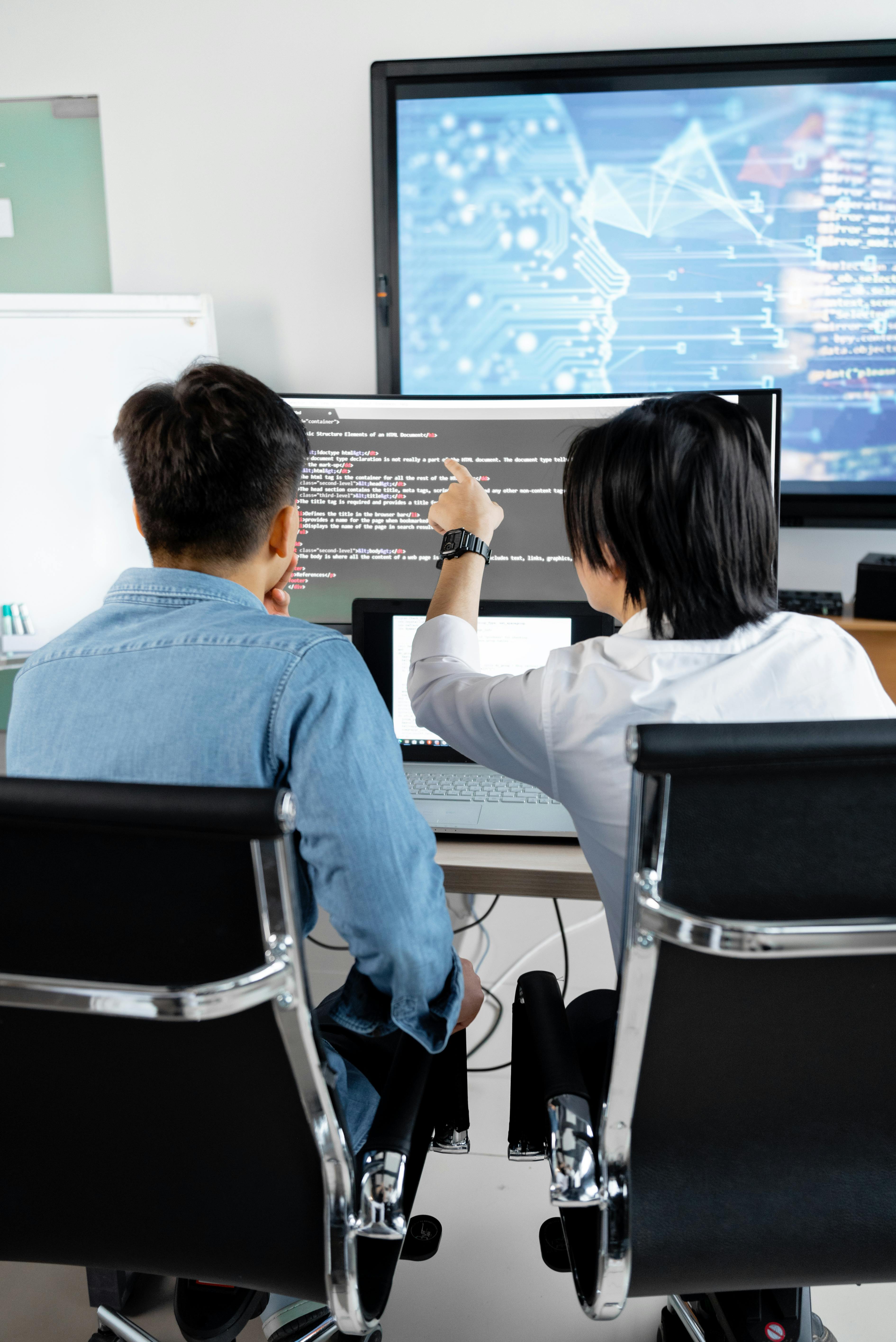 Two students reviewing HTML on a large monitor in a modern STEM lab with a wall display. Photo: Mikhail Nilov / Pexels.