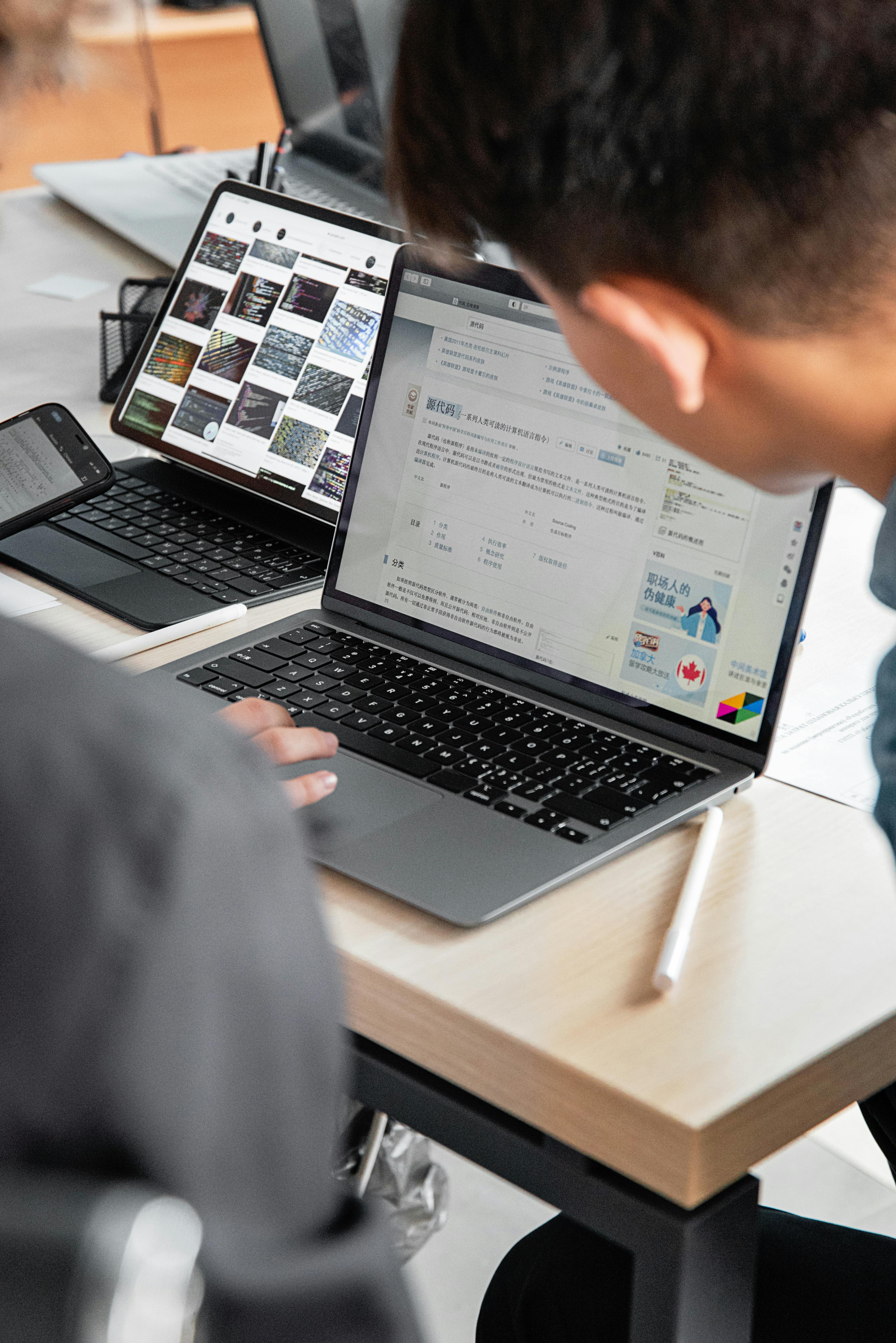 Over-the-shoulder view of laptop, tablet, and phone showing study and technical content on desk. Photo: Mikhail Nilov / Pexels.