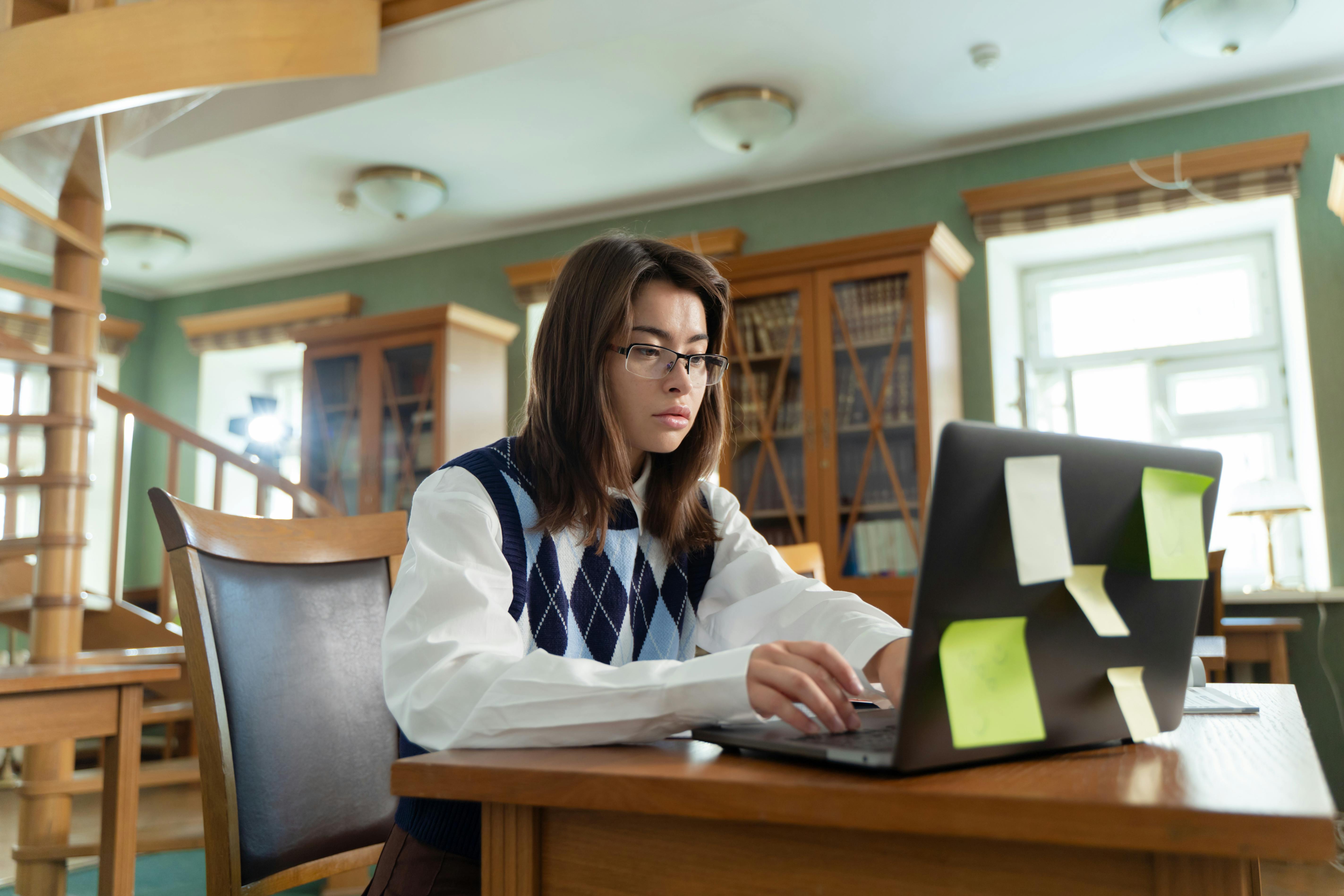 Student working on a laptop in a library with study notes. Photo: Yaroslav Shuraev / Pexels.